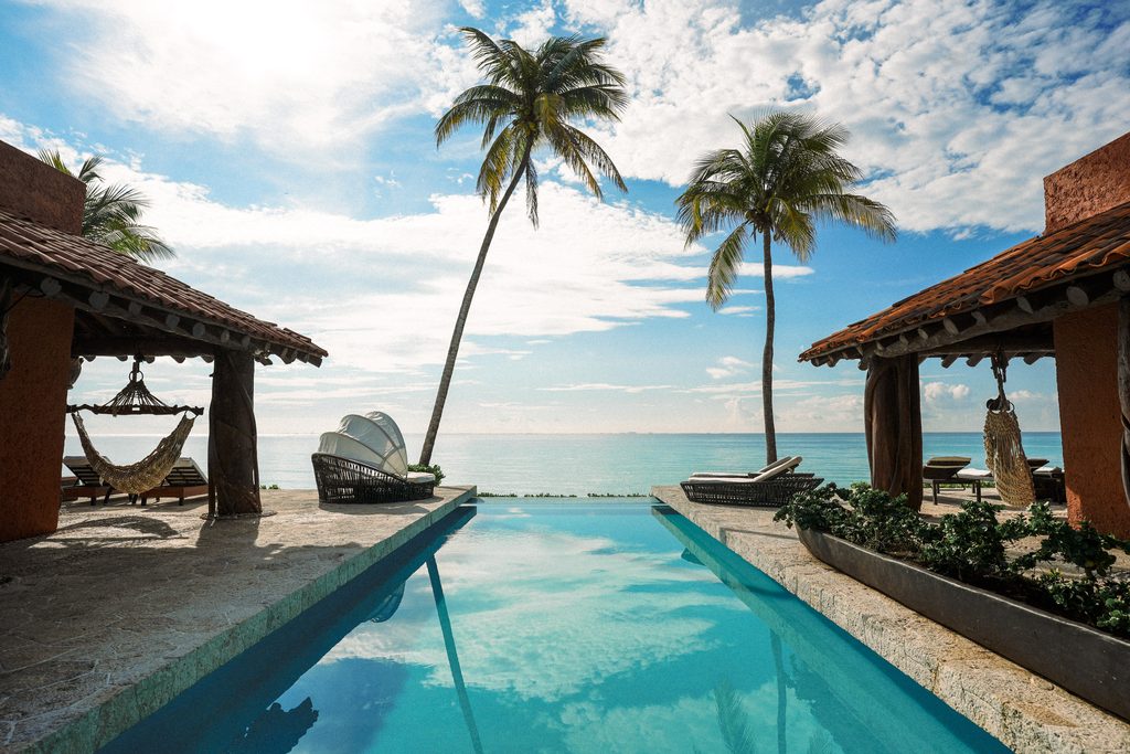 Alberca infinita frente al Mar Caribe con palapa y palmeras en Casa Corazón, Playacar